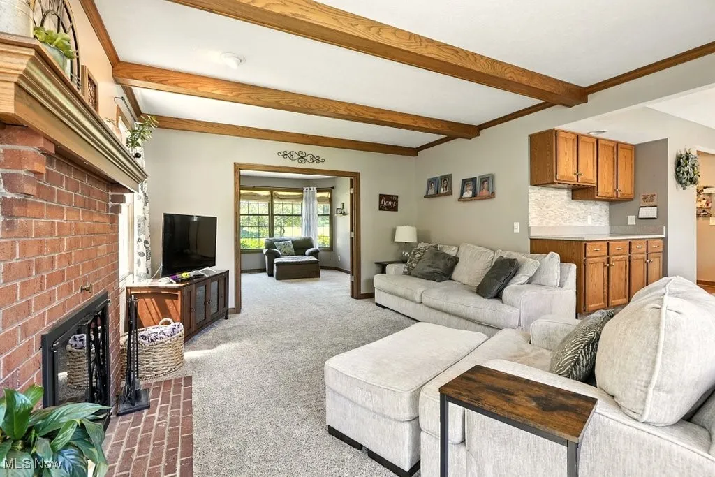 Carpeted living area with a brick fireplace, beam ceiling, and ornamental molding