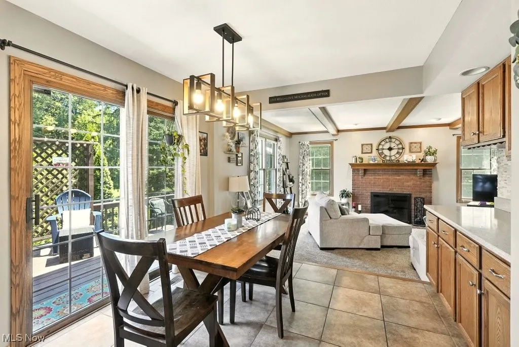 Dining space featuring beam ceiling, light tile patterned floors, and a brick fireplace