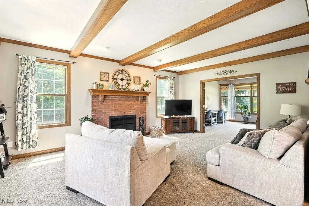 Carpeted living area featuring beamed ceiling and a fireplace