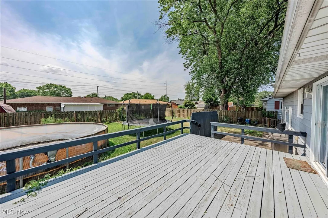 Wooden terrace with a trampoline and a fenced backyard