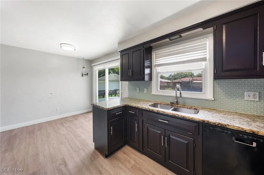 Kitchen featuring black dishwasher, backsplash, light wood-style floors, and light stone countertops