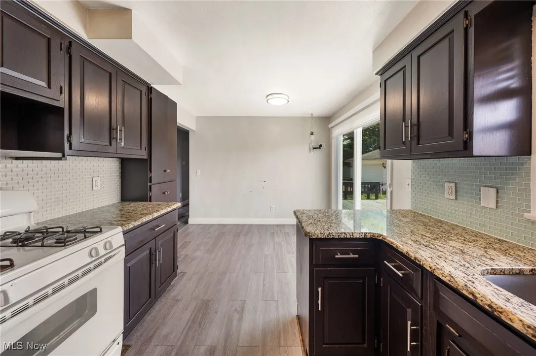 Kitchen with white range with gas stovetop, light wood finished floors, tasteful backsplash, and light stone counters