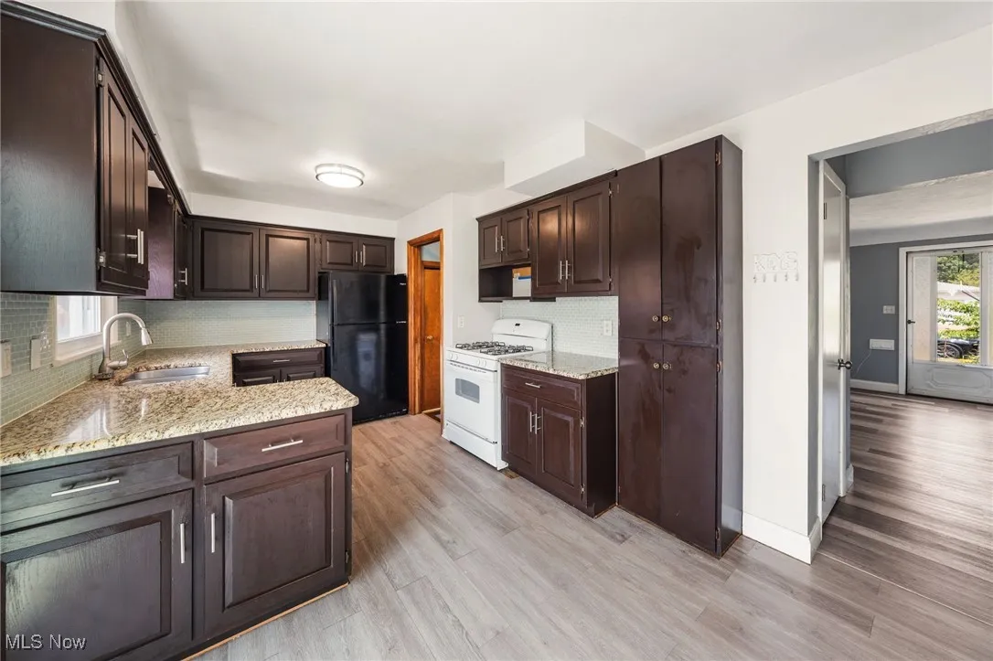 Kitchen featuring white range with gas stovetop, freestanding refrigerator, dark brown cabinetry, and light wood-style flooring