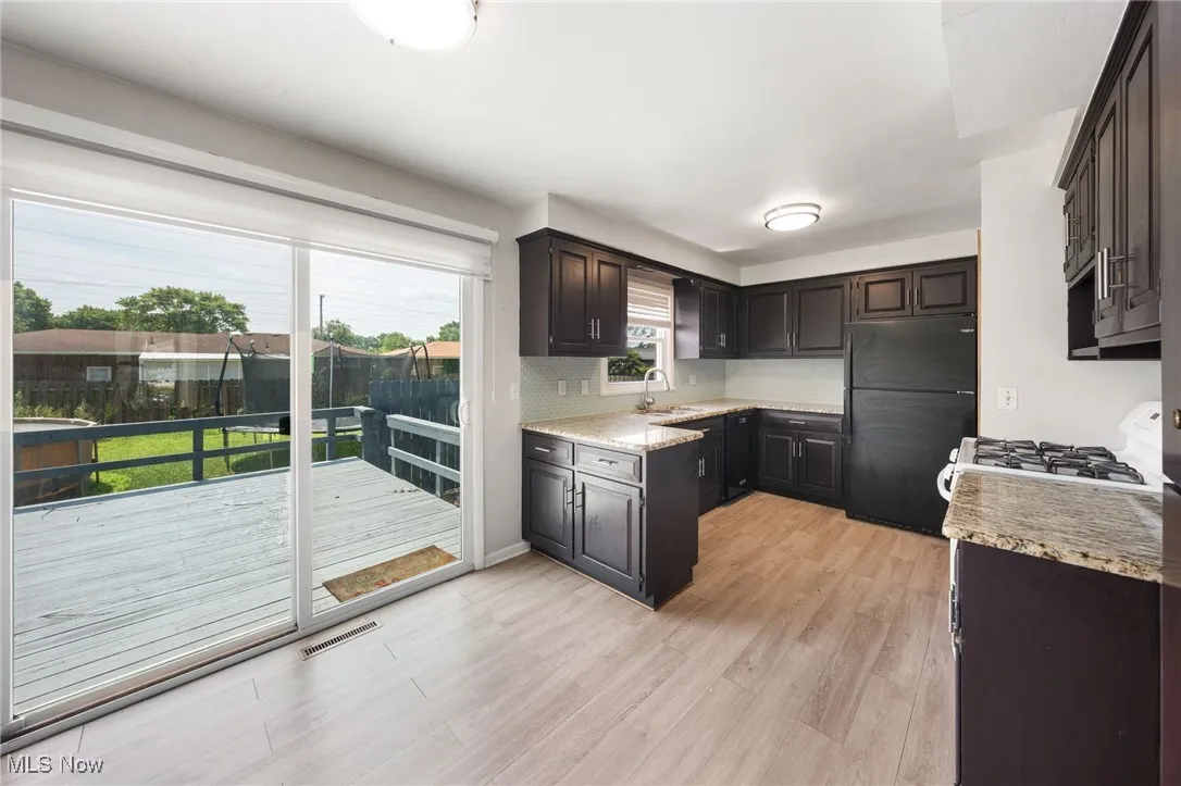 Kitchen with white gas range, freestanding refrigerator, light wood-style flooring, light stone countertops, and dark brown cabinetry