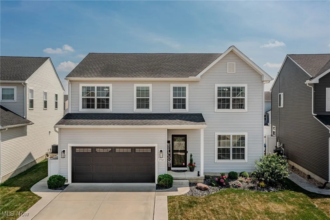 Traditional-style home with a shingled roof, concrete driveway, a garage, and a front yard