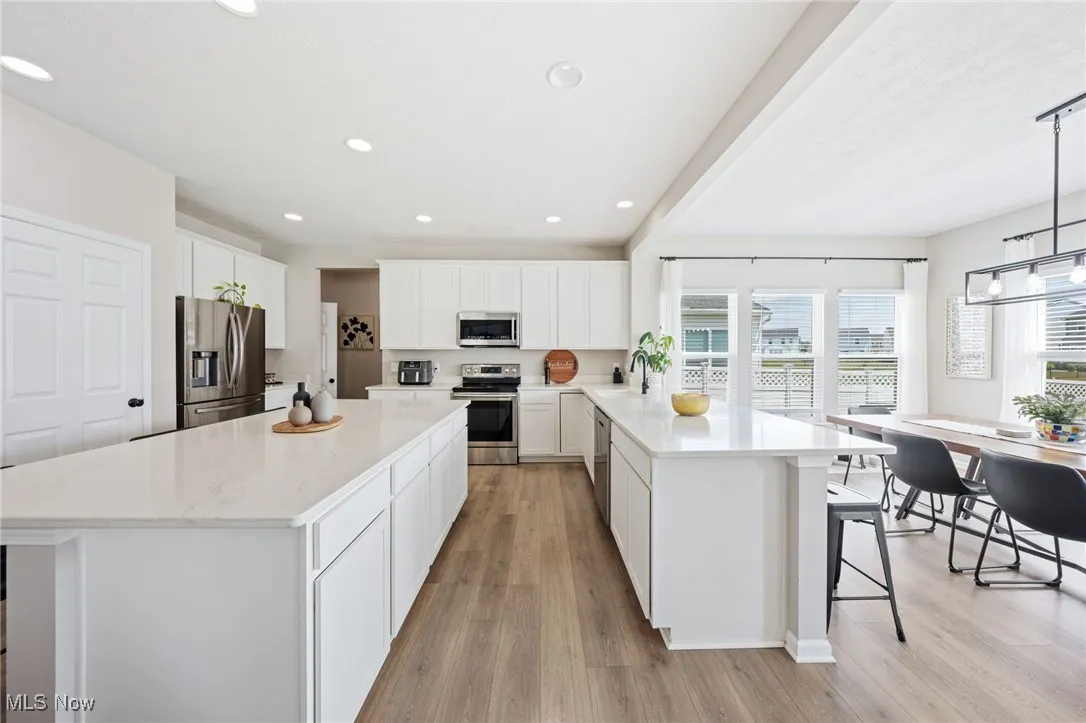Kitchen with appliances with stainless steel finishes, a peninsula, light wood-style floors, a breakfast bar area, and white cabinetry