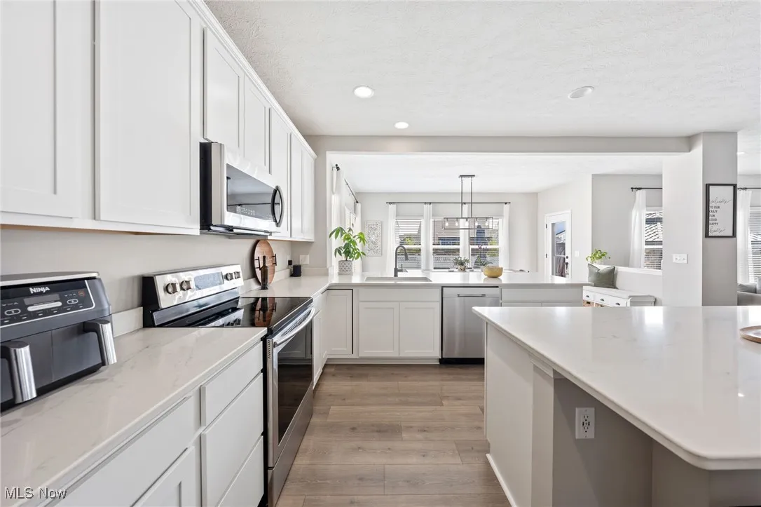 Kitchen with appliances with stainless steel finishes, a peninsula, light wood-style floors, white cabinets, and recessed lighting