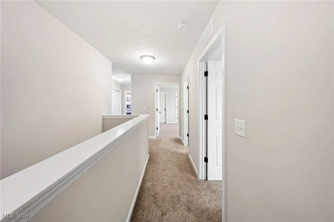 Hall featuring light carpet, a textured ceiling, and an upstairs landing