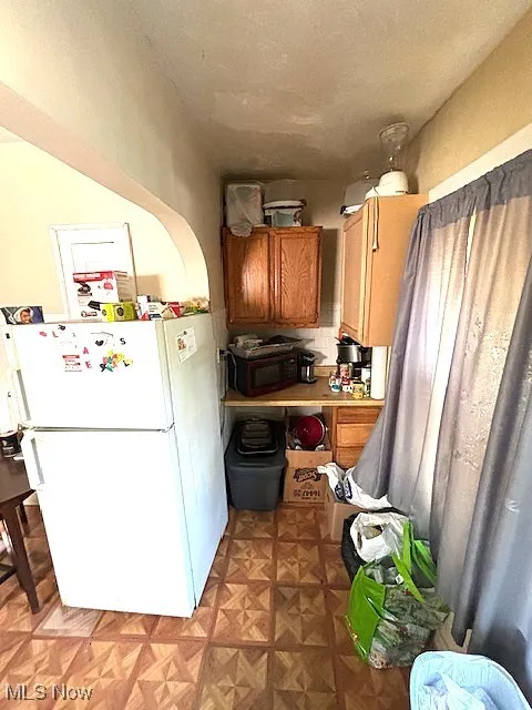 Kitchen featuring freestanding refrigerator, brown cabinetry, and black microwave