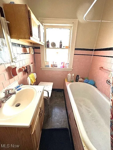 Full bath with a bath, vanity, tile walls, and a wainscoted wall