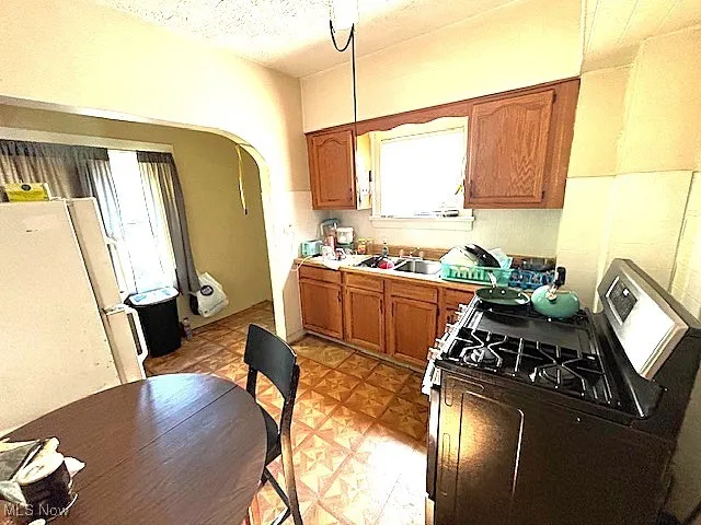 Kitchen with stainless steel range with gas stovetop, brown cabinetry, healthy amount of natural light, freestanding refrigerator, and a textured ceiling