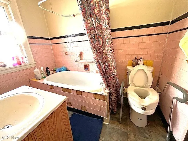 Full bathroom featuring tile walls, tiled shower / bath combo, wainscoting, and vanity