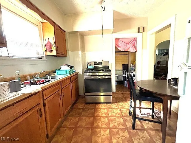 Kitchen featuring gas stove, brown cabinetry, freestanding refrigerator, light countertops, and light flooring