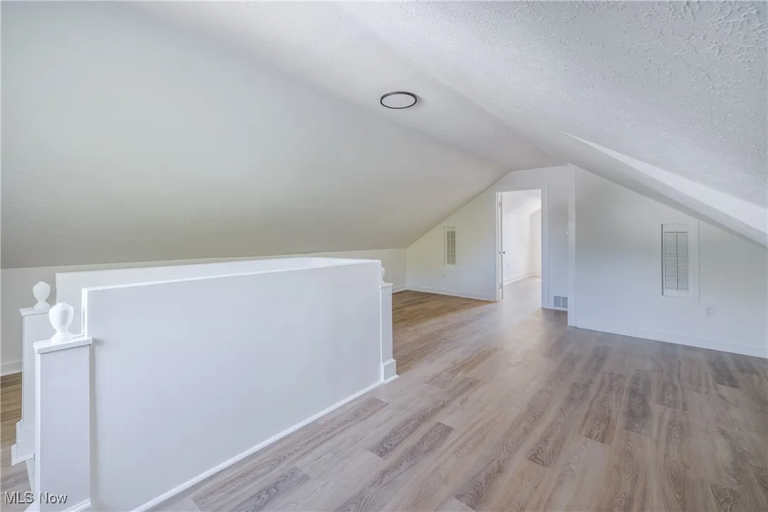 Bonus room featuring vaulted ceiling, light wood-style floors, and a textured ceiling