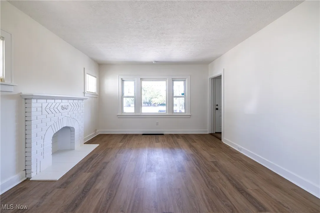 Unfurnished living room featuring a textured ceiling, healthy amount of natural light, dark wood-style floors, and a brick fireplace