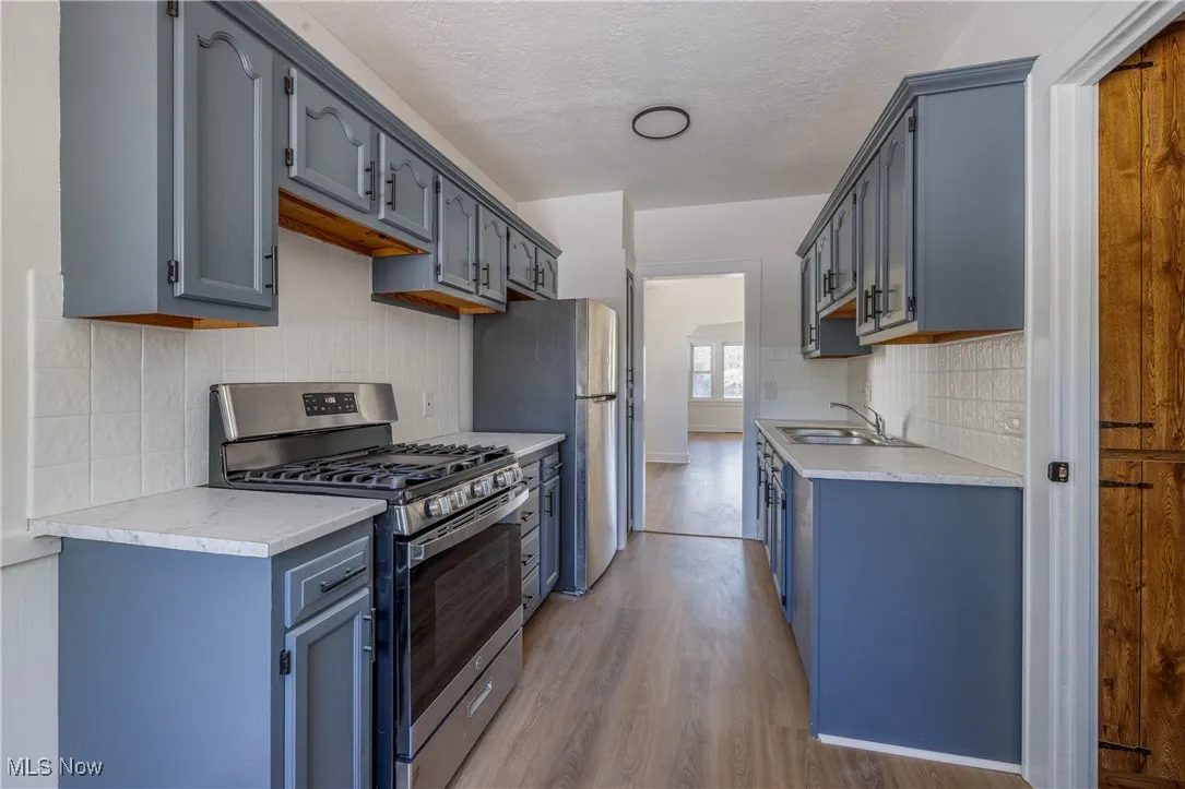 Kitchen featuring stainless steel appliances, light wood-style floors, light countertops, a textured ceiling, and backsplash