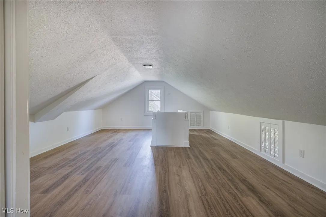 Additional living space featuring a textured ceiling, dark wood finished floors, and vaulted ceiling