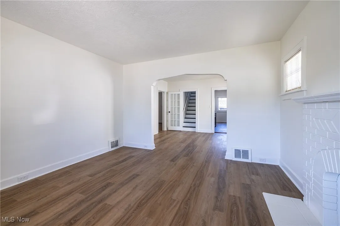Empty room featuring arched walkways, dark wood finished floors, a textured ceiling, and stairway