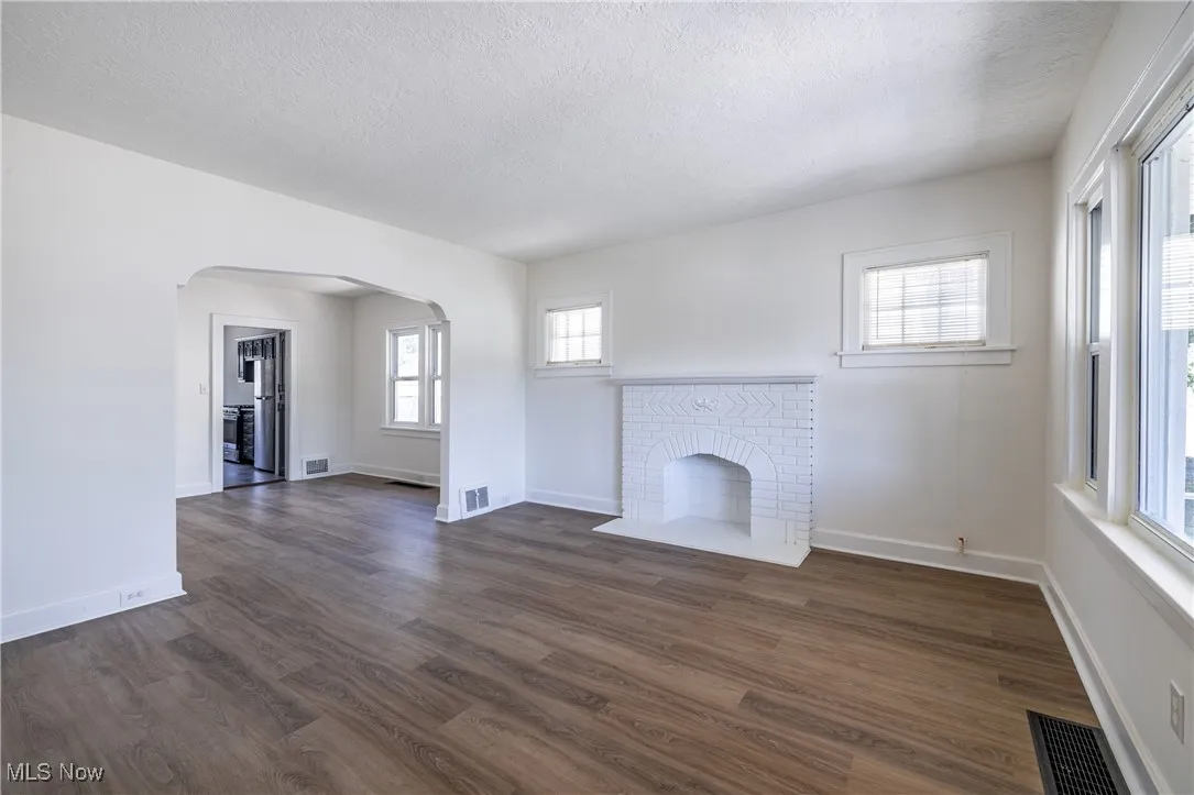 Unfurnished living room featuring arched walkways, a textured ceiling, dark wood-style floors, and a brick fireplace