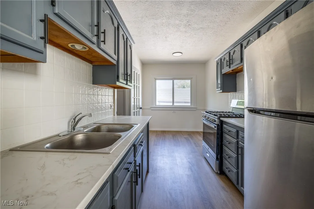 Kitchen with stainless steel appliances, dark wood finished floors, decorative backsplash, a textured ceiling, and light countertops