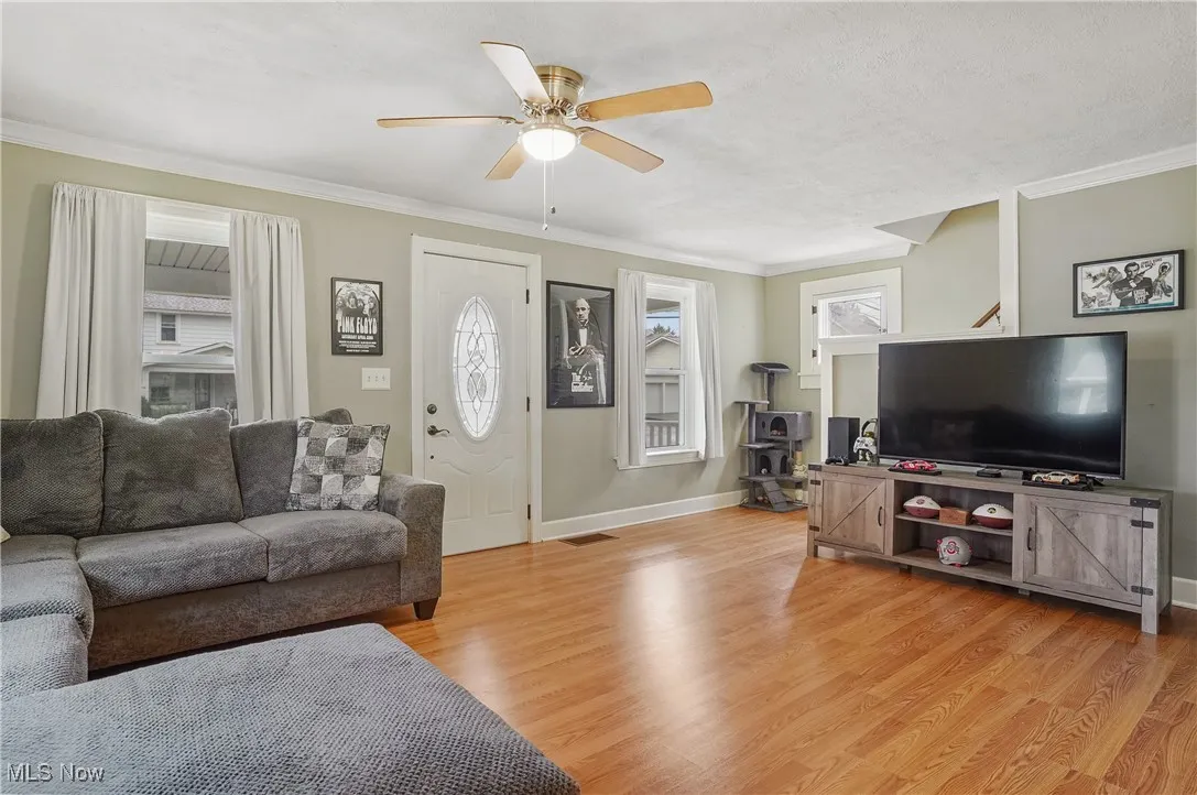 Living room with ceiling fan, light wood-style floors, and crown molding