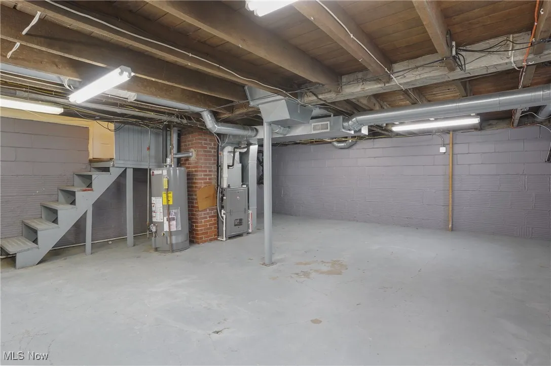 Unfinished below grade area featuring stairway, gas water heater, heating unit, and concrete block wall