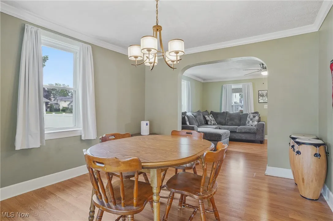 Dining space with arched walkways, light wood finished floors, a chandelier, ornamental molding, and ceiling fan
