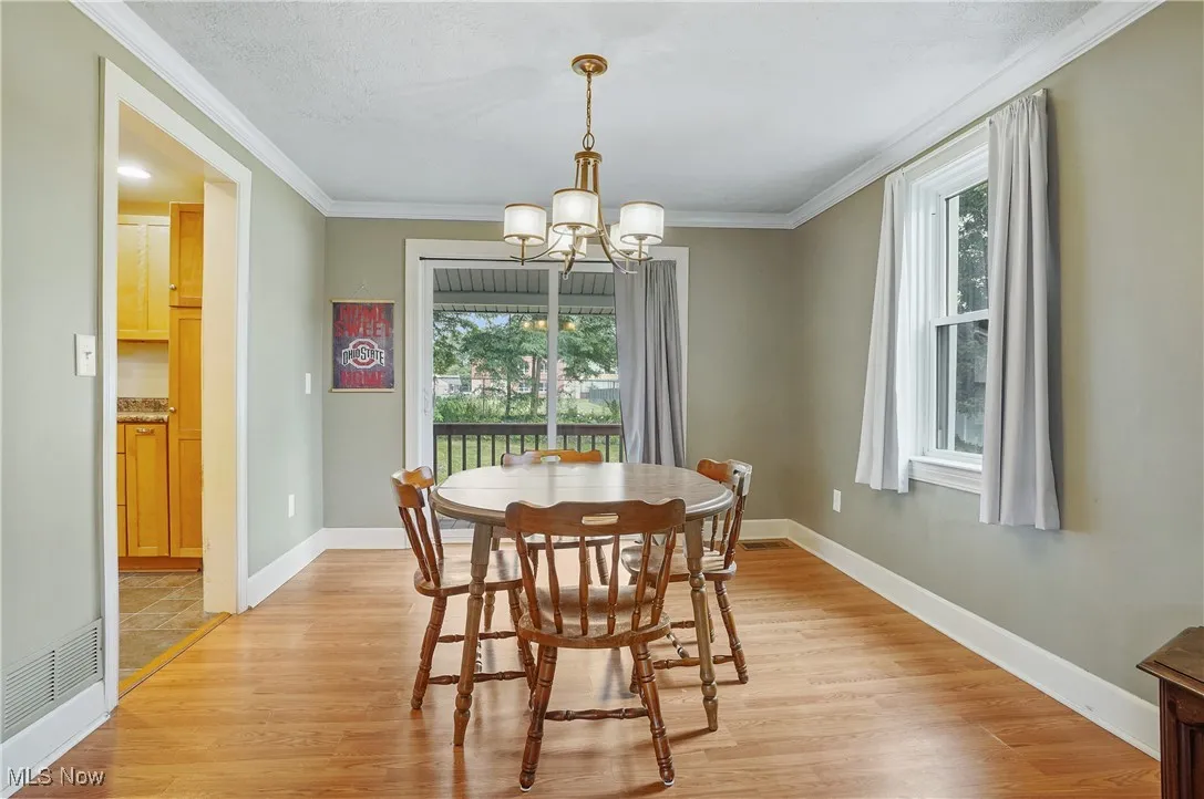 Dining room featuring healthy amount of natural light, light wood-style floors, a chandelier, and crown molding
