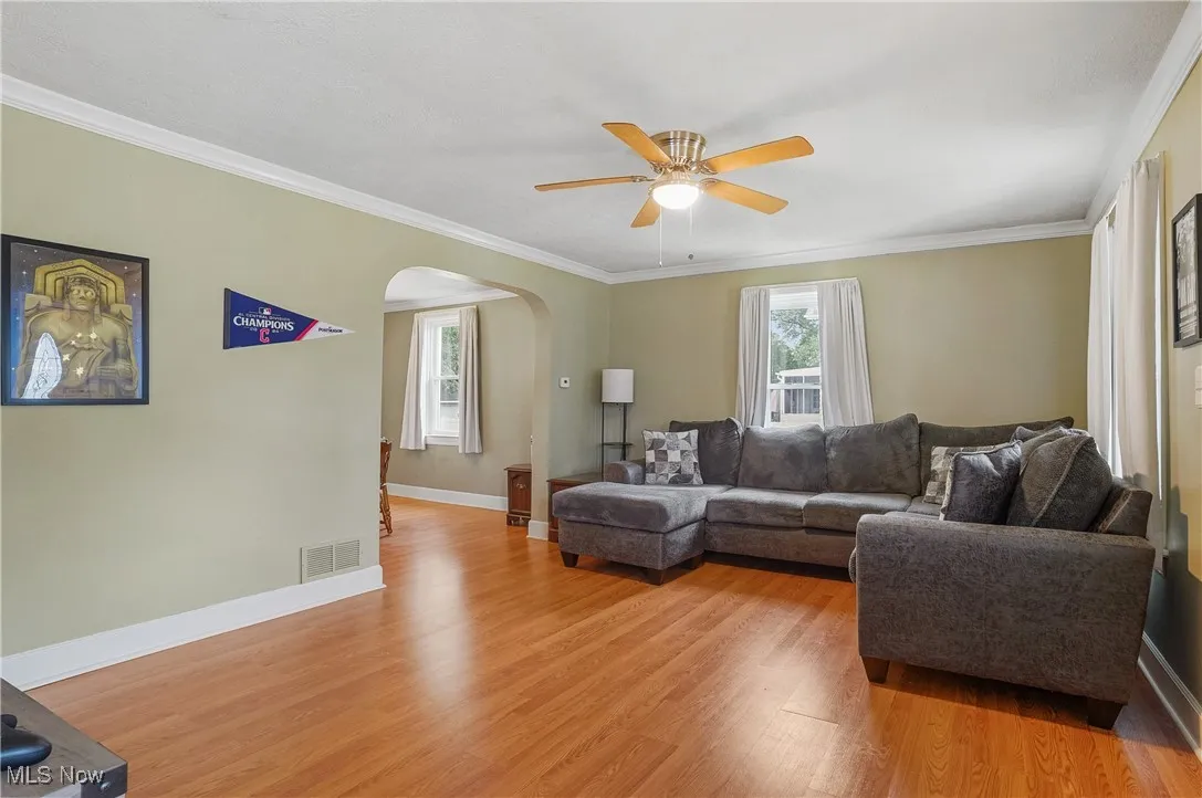 Living area featuring arched walkways, light wood-type flooring, a ceiling fan, and ornamental molding