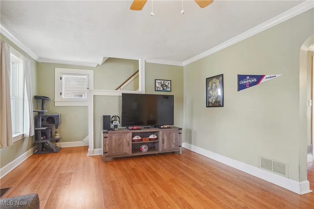 Living area with a wood stove, light wood-style floors, arched walkways, ceiling fan, and crown molding