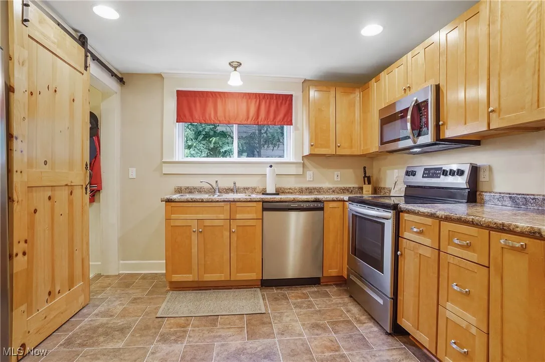 Kitchen with stainless steel appliances, a barn door, light stone finish flooring, and recessed lighting