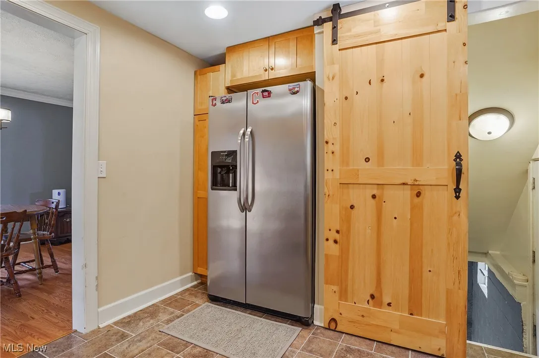 Kitchen with stainless steel refrigerator with ice dispenser, crown molding, and a barn door