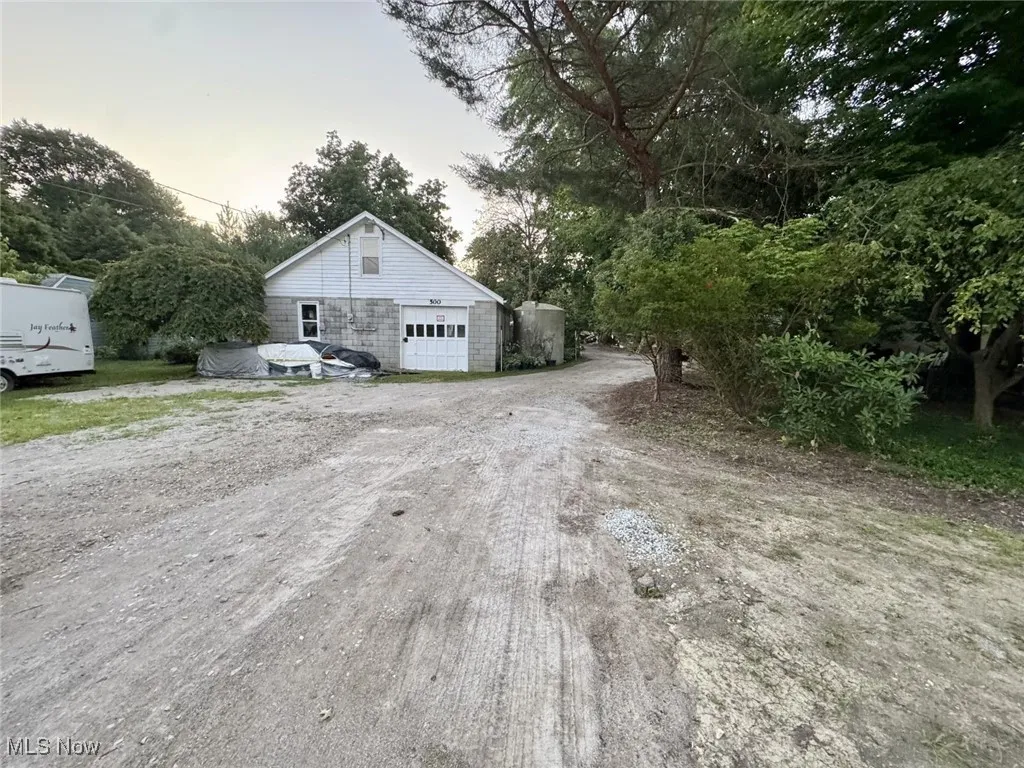 Property exterior at dusk with a garage, dirt driveway, an outbuilding, and view of wooded area