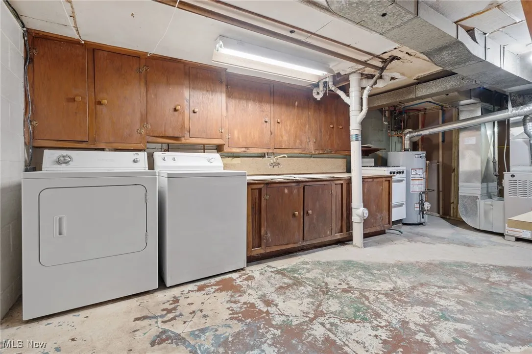 Washroom featuring washing machine and clothes dryer, cabinet space, water heater, and heating unit