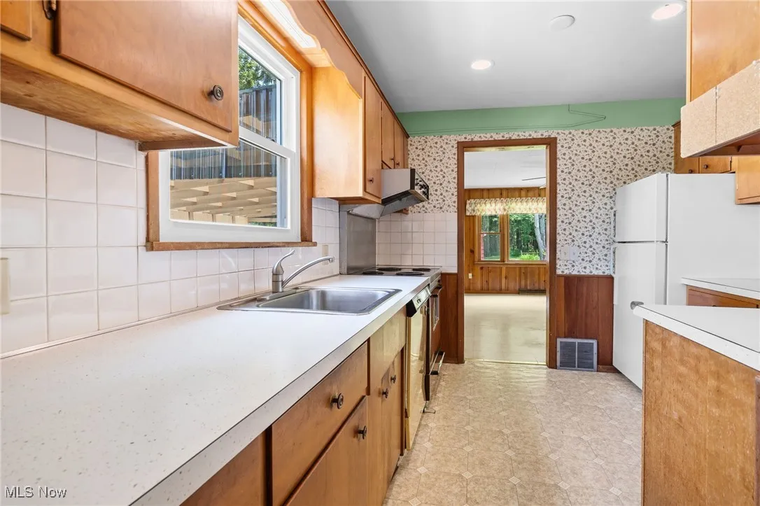 Kitchen with light countertops, freestanding refrigerator, backsplash, stove, and brown cabinets