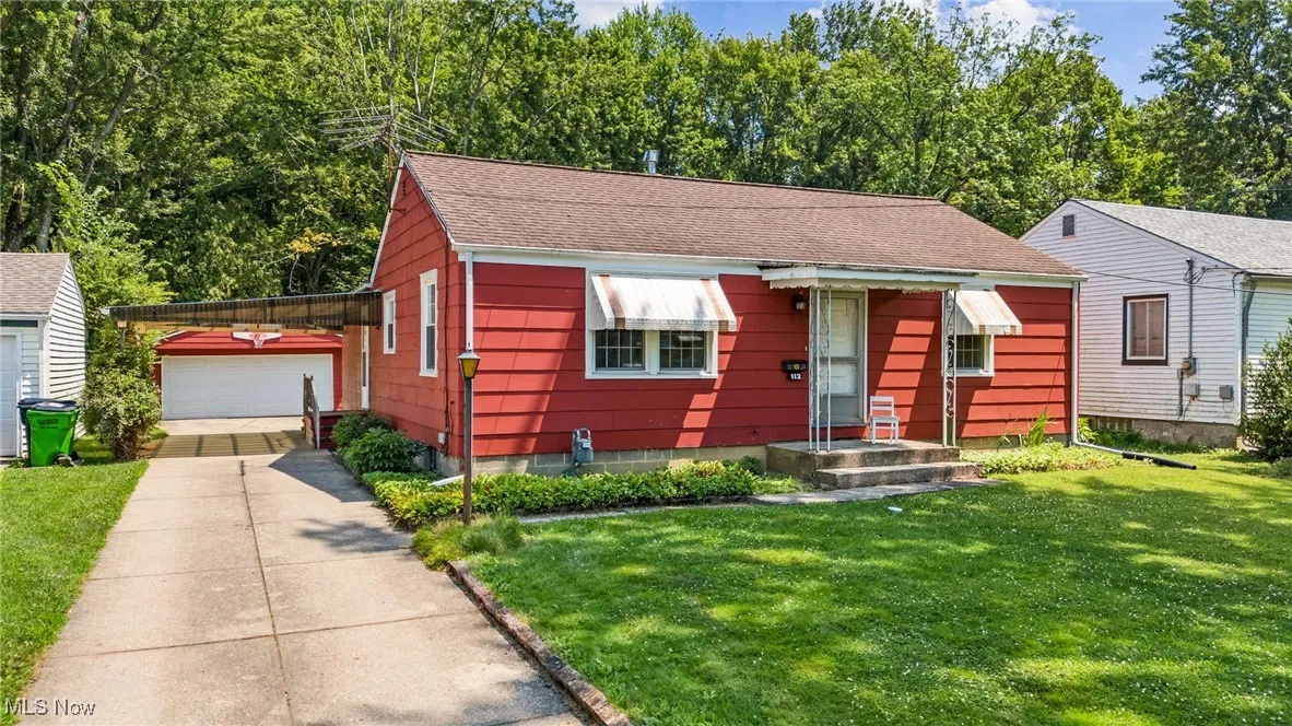 View of front of property featuring an outdoor structure, a shingled roof, a front yard, and driveway