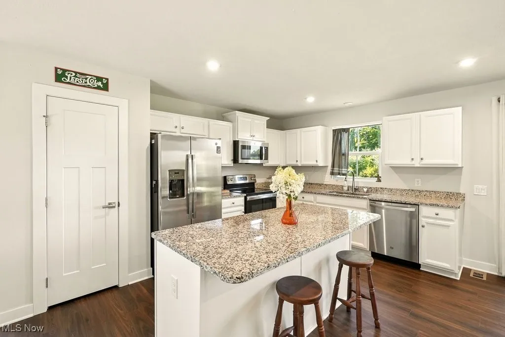 Kitchen featuring stainless steel appliances, dark wood-style floors, white cabinetry, a center island, and light stone countertops