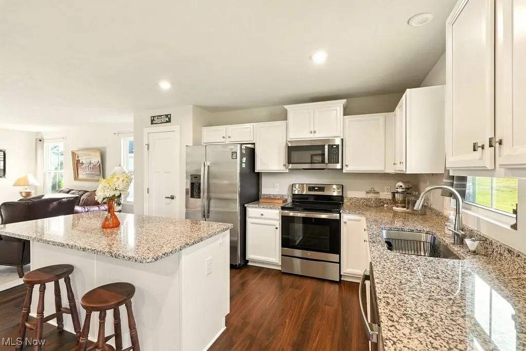Kitchen featuring appliances with stainless steel finishes, a breakfast bar, dark wood finished floors, light stone countertops, and white cabinets