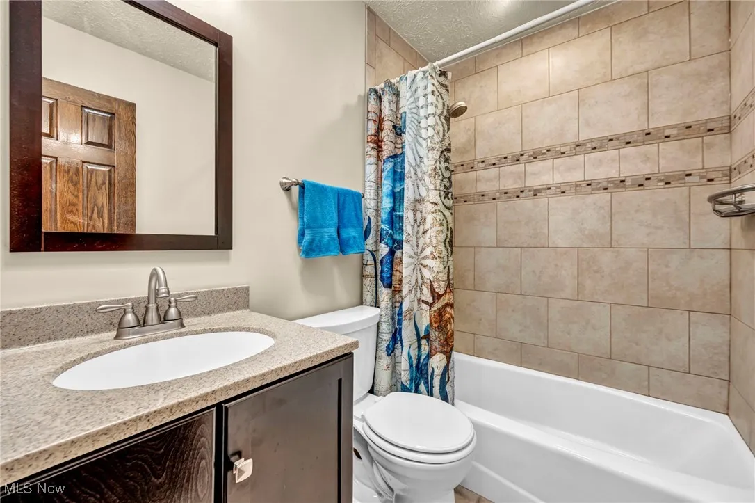 Bathroom with vanity, a textured ceiling, and shower / bathtub combination with curtain