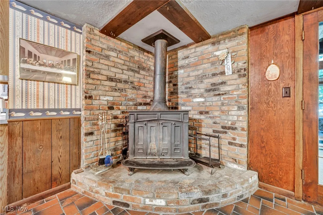 Detailed view of a textured ceiling, a wood stove, wooden walls, wallpapered walls, and beamed ceiling