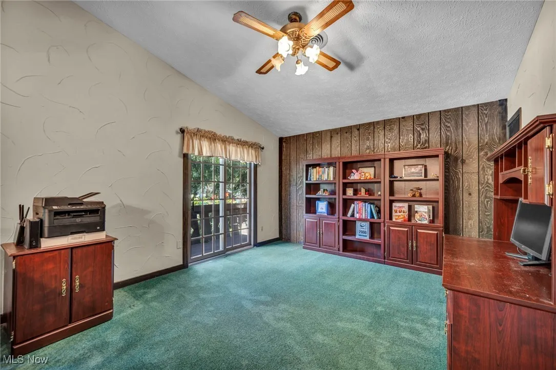 Unfurnished office featuring lofted ceiling, ceiling fan, carpet flooring, and a textured ceiling