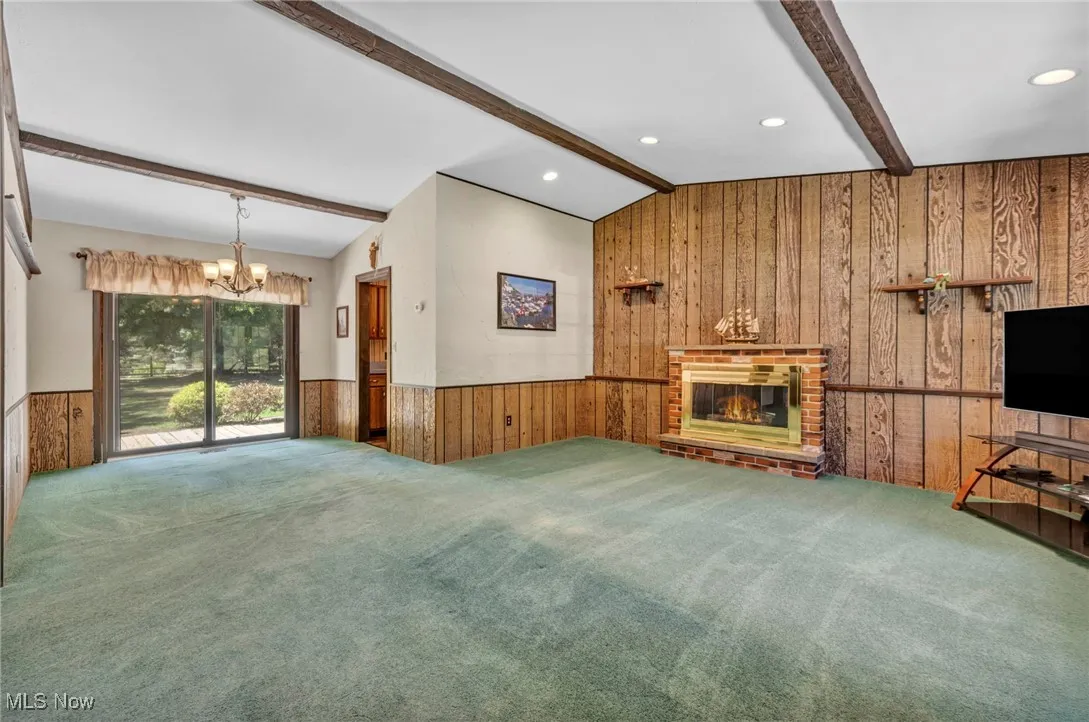 Unfurnished living room with wood walls, a fireplace, a chandelier, carpet flooring, and wainscoting