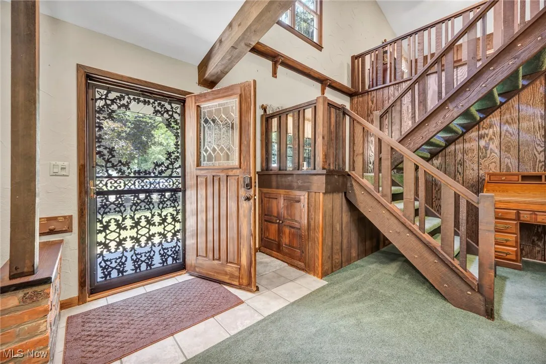 Foyer entrance featuring stairs, carpet flooring, beamed ceiling, tile patterned flooring, and high vaulted ceiling