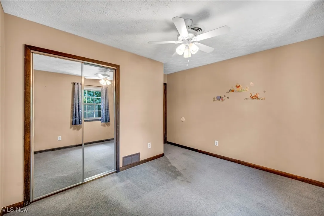 Carpeted empty room with ceiling fan and a textured ceiling