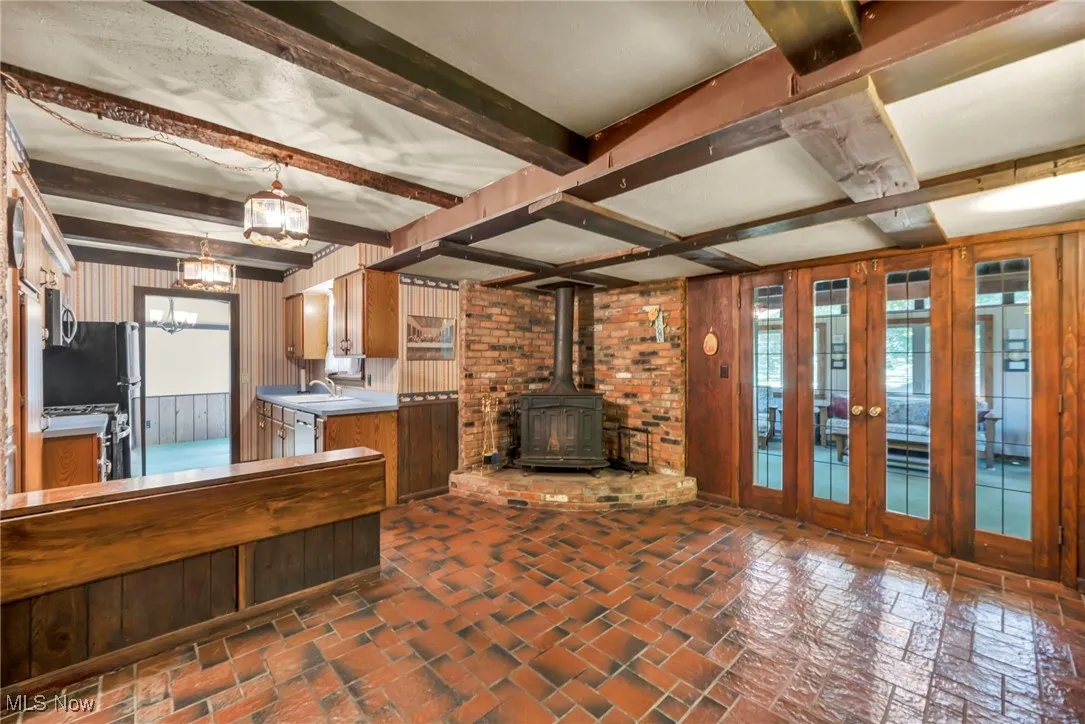 Kitchen featuring brick floors, beam ceiling, a wood stove, appliances with stainless steel finishes, and wood walls