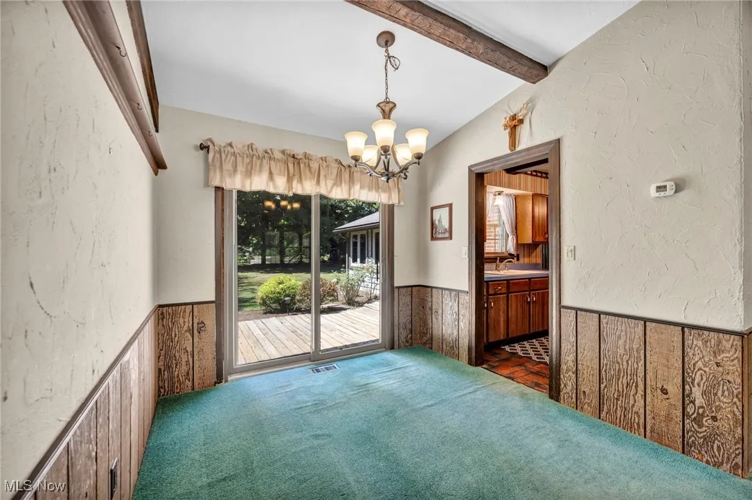 Unfurnished room with wainscoting, wood walls, a chandelier, a textured wall, and dark colored carpet
