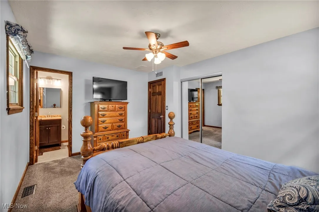 Bedroom with light carpet, a closet, ceiling fan, and connected bathroom