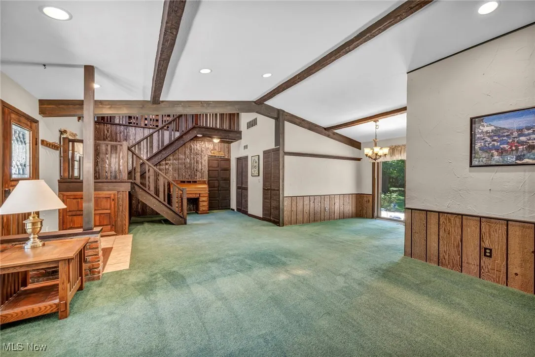 Unfurnished living room with a wainscoted wall, wood walls, carpet flooring, stairs, and a chandelier