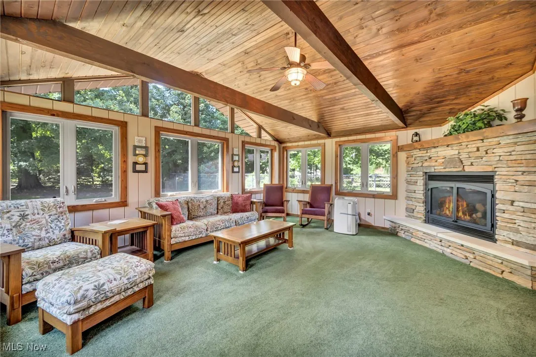 Living area featuring carpet flooring, a ceiling fan, a stone fireplace, and wooden ceiling