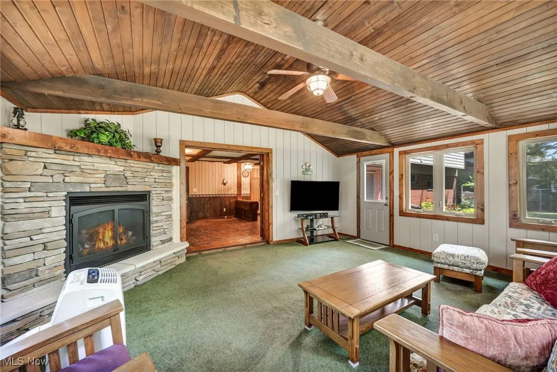 Living room with carpet flooring, a stone fireplace, a ceiling fan, wooden ceiling, and wooden​​‌​​​​‌​​‌‌​‌‌​​​‌‌​‌​‌​‌​​​‌​​ walls